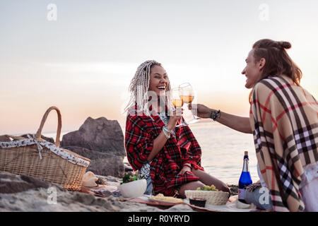 Young couple with plaids on shoulders having romantic dinner on the beach Stock Photo