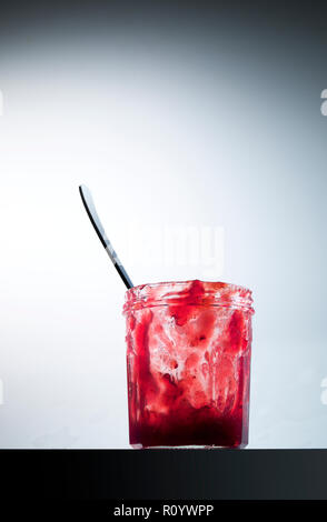 Red jam in nearly empty jam jar with dessert spoon, still life Stock Photo