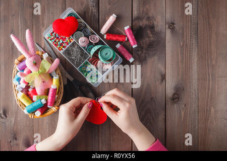 Woman sews red heart shaped toy by needle, conceptual symbol of love Stock Photo