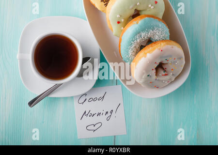 Four donuts on old wood table with cup and note "Good morning" Stock Photo