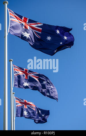 Three Australian National Flags each atop a white flagpole on a clear blue sky, memorial day. Stock Photo