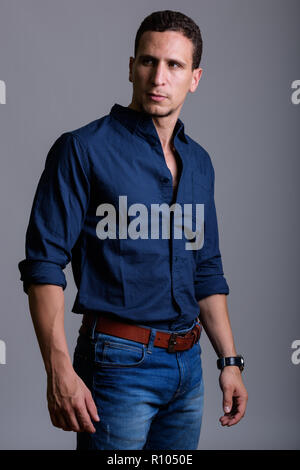 Studio shot of young muscular Persian man standing while thinkin Stock Photo