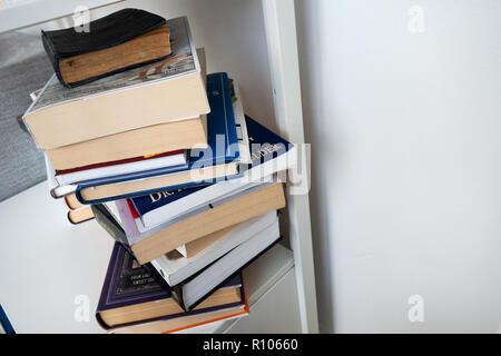 photograph of the sides of a pile of hardbacked and paperback books on a white shelf, no copy Stock Photo