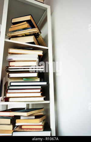 photograph of the sides of a pile of hardbacked and paperback books on a white shelf, no copy Stock Photo