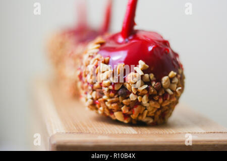 Three bright red candy apples with nuts on natural wood board and grey background Stock Photo