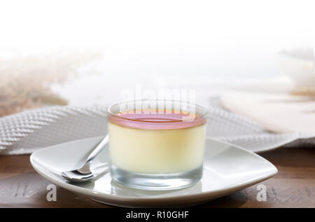 Close up of glass pudding creme caramel on plate with spoon, white tablecloth Stock Photo
