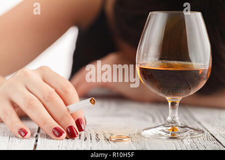 Drunk woman holding an alcoholic drink and sleeping with her head on the table (Focused on the drink, her face is out of focus) Stock Photo