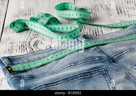 Blue jeans and measuring tape in waistband and in body on wood background Stock Photo