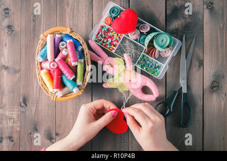 Woman sews red heart shaped toy by needle Stock Photo