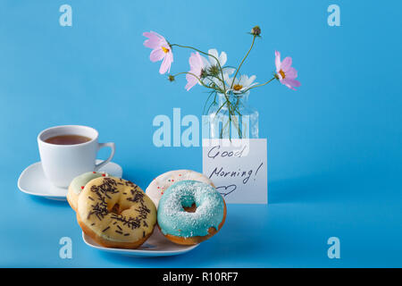 Concept beakfat. Donuts on saucer with cup of tea, flowers  and note "Good morning" Stock Photo