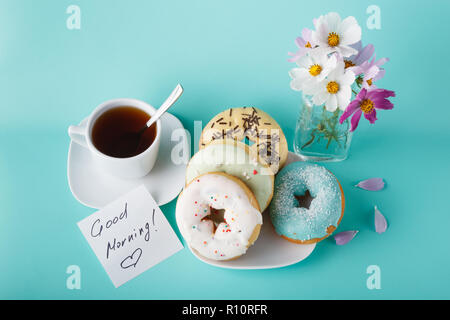 Four donuts on saucer with cup of tea. Aquamarine background Stock Photo