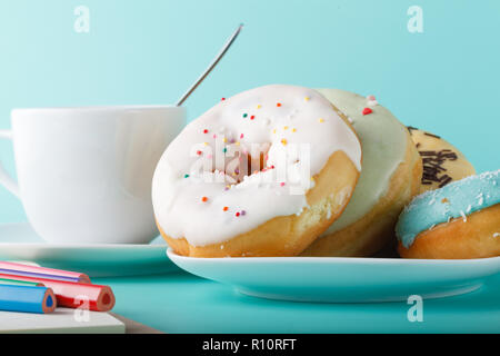 Four donuts on saucer with cup of tea. Aquamarine background Stock Photo