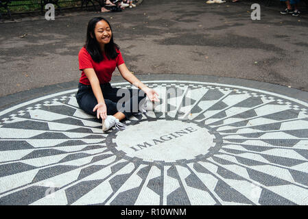 New York City, USA - June 23, 2018: Young Asian woman sitting on the Imagine mosaic in the Strawberry Fields in Central Park. Stock Photo