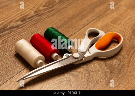 Coulourful red white green thread spools and pair of scissors on wooden work bench Stock Photo