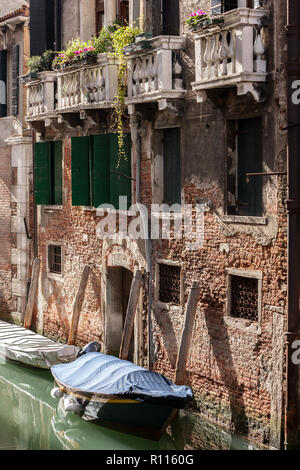 Old brick and painted buildings with balconies and doorways with covered  gondala boats on the canals of Venice Italy Stock Photo