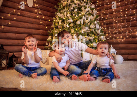 The kids are sitting under the Christmas tree. Brothers and sisters are sitting under the tree waiting for gifts. New Year's and Christmas. Stock Photo
