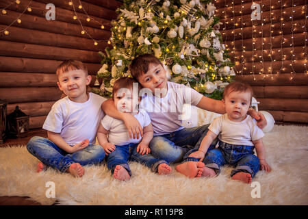 The kids are sitting under the Christmas tree. Brothers and sisters are sitting under the tree waiting for gifts. New Year's and Christmas. Stock Photo