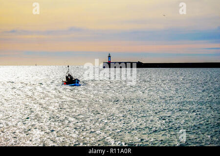 Fishing boat entering Newhaven harbour, Newhave harbour ighthouse is behind at the end of the harbour wall the wall is jutting out from the right hand Stock Photo