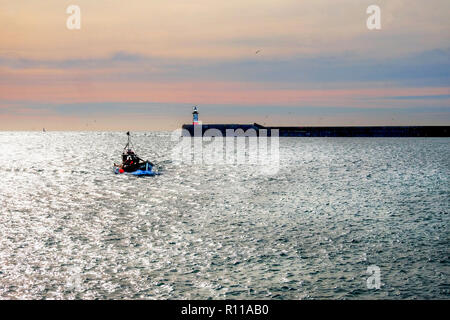 Fishing boat entering Newhaven harbour, Newhave harbour ighthouse is behind at the end of the harbour wall the wall is jutting out from the right hand Stock Photo