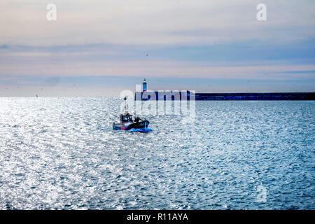 Fishing boat entering Newhaven harbour, Newhave harbour ighthouse is behind at the end of the harbour wall the wall is jutting out from the right hand Stock Photo