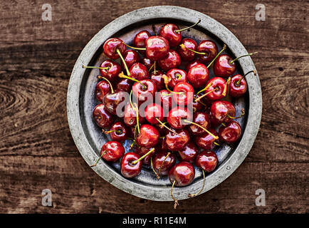 A metallic rustic bowl full of ripe Cherries over a wooden table. Stock Photo