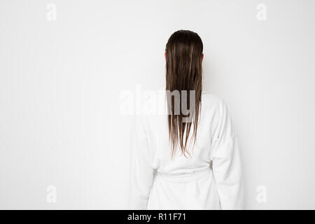 back of a young woman showing her wet hair to camera in bathrobe on white background Stock Photo