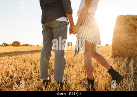 Cropped photo of guy and girl walking through golden field with bunch of haystacks during sunny day Stock Photo