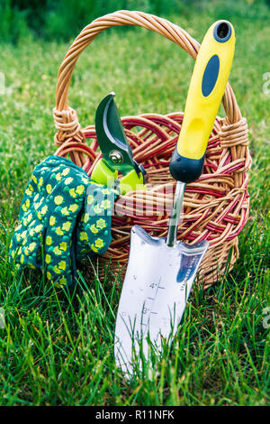 Small hand garden trowel, pruner and gloves with wicker basket in green grass. Garden tools and equipment Stock Photo