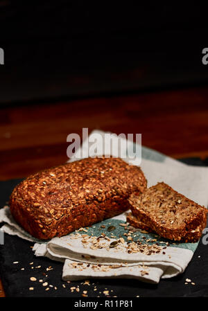 Freshly made oat, sunflower, flax, pumpkin, sesame and rye seed whole grain bread on black stone cutting board, sprinkled with sesame seeds. Very shal Stock Photo