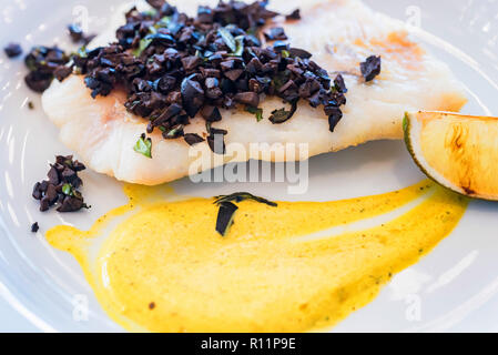 Pike perch fillet with vegetables and olives on white plate Stock Photo
