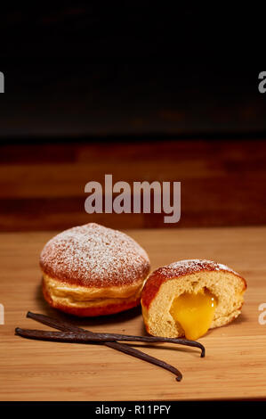 Freshly made vanilla filled doughnuts on wooden cutting board. Very shallow depth of field Stock Photo