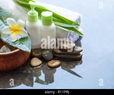 Spa or wellness setting with bowl of water with flower, towel and cream tubes on dark background Stock Photo