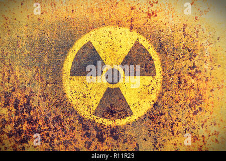 Round yellow radioactive (ionizing radiation) danger symbol painted on a massive rusty metal wall with rustic grunge texture background. Washed fading Stock Photo