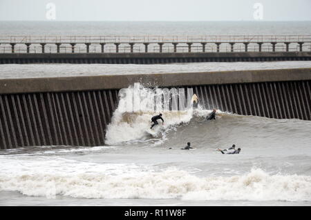 Surfing a 'man made' wave off a harbour wall in  Swansea bay close to the location of proposed Tidal Barrage a group of surfers wait their turn Stock Photo