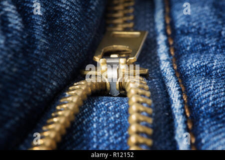 Unzipped brass zipper closeup on blue jeans Stock Photo
