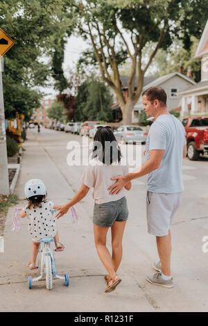 Family walking with daughter on tricycle Stock Photo
