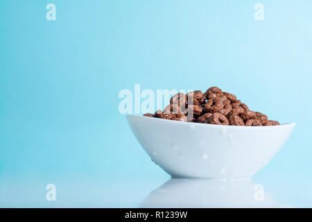 Chocolate flakes in the form of rings in white bowl on a light blue celestial sky background Stock Photo