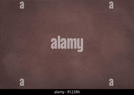 Dark brown matte background of suede fabric, closeup. Velvet texture of seamless deep umber leather with vignette. Felt materisl macro. Stock Photo