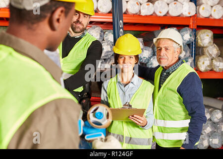 Workers as a logistics team in the warehouse discuss a delivery together Stock Photo