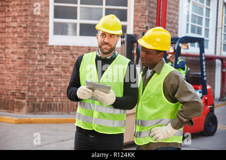 Two warehouse workers using tablet computer together in front of the logistics center Stock Photo
