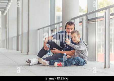 Little boy and his father taking a break and listening to the music together in a sports center. Father and son spend time together and lead a healthy Stock Photo