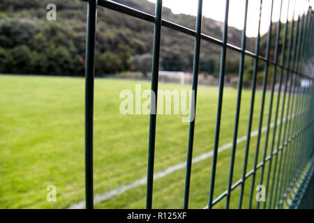 Detail of a soccer field with white line and fence / Close up metallic net-shaped green fence on a background of football field. Stock Photo