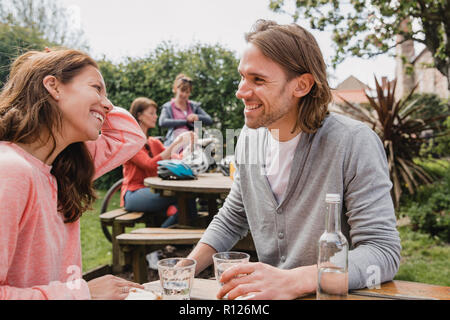 Mid-adult couple sitting at a bench outdoors in a public park. They are looking at each other, smiling, laughing and talking. Stock Photo