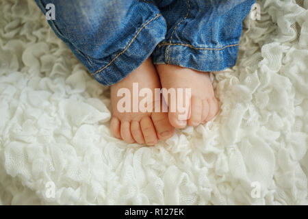 legs fashionable newborn baby. Little child in jeans sleeping in white blanket, lying on bed. Stock Photo