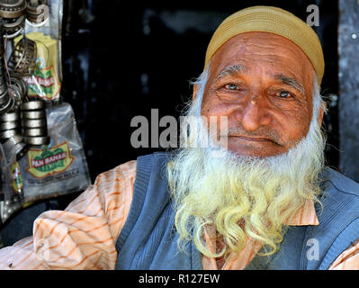 Old Indian Muslim man with a white, long and bushy full beard, wears a knitted mustard-yellow Islamic skull cap (taqiyah) and poses for the camera. Stock Photo