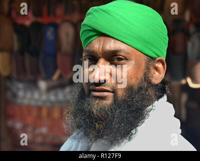 Afghani shoe merchant with black Islamic beard wears a turban-style headdress in green and poses for the camera. Stock Photo