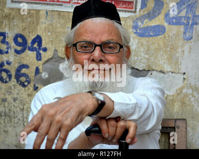 Sitting elderly Indian Muslim man with a white Islamic beard wears his traditional white Islamic clothing and a black skull cap (taqiyah). Stock Photo