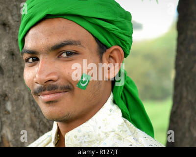 Young Indian Muslim man with a green Islamic flag painted on his face wears a green headscarf during the Rabi' al-awwal festivities. Stock Photo