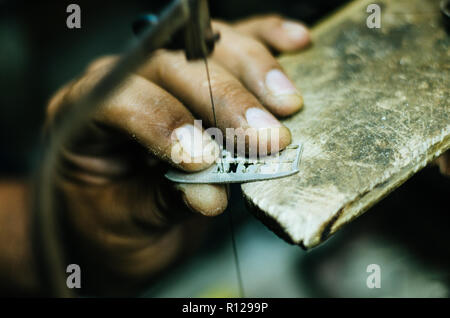 man's hands goldsmith work on a piece of silver with a metal saw on the work table, close up, selected focus, narrow depth of field Stock Photo