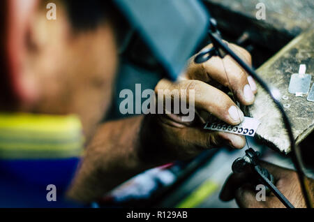 man's hands goldsmith work on a piece of silver with a metal saw on the work table, close up, selected focus, narrow depth of field Stock Photo